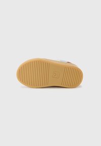 Semelle en caoutchouc d'une sneaker, avec une surface texturée et des rainures. La couleur est beige avec un logo embossé sur le talon.