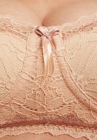 Lace-bh i myk beige med delikat blomstermønster, som har en satengbåndsløkke i midten og intrikate blonderkant langs kantene.