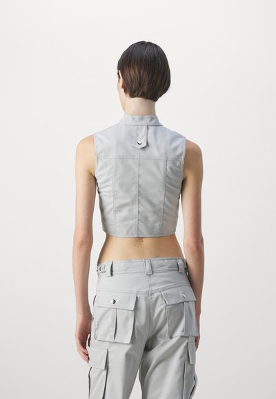 Gray cropped sleeveless top made of smooth fabric, featuring a pointed collar and back button detail. Worn with matching cargo pants.