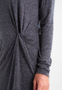 Dunkelgraues Langarmkleid aus strukturiertem Stoff, mit einem verdrehten Detail an der Taille und weichem, fallendem Material.