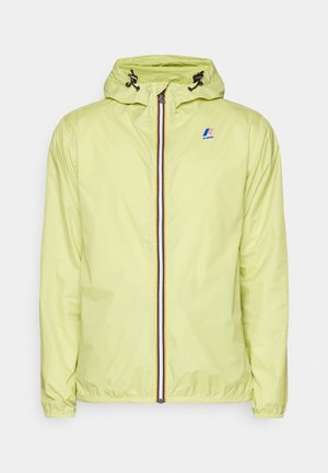 Coupe-vent à capuche jaune clair avec fermeture éclair à l'avant et poignets élastiques, avec un petit logo K-Way sur la poitrine.