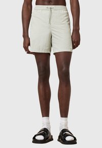 Light green shorts with an elastic waistband and drawstring. Made of fabric with a smooth texture. Black sandals with two buckles and white socks.