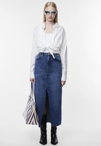 Fehér, hosszú ujjú ing, a deréknál megkötve, kék farmer szoknya elülső réssel, fekete bokacsizma és csíkos válltáska.