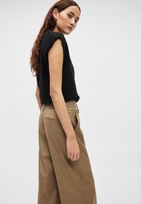 Czarny, dzianinowy top bez rękawów w połączeniu z wysokim stanem, szerokimi, beżowymi spodniami o gładkiej fakturze i bocznych kieszeniach.
