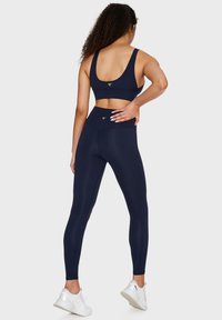 Marinblå sömlös sport-bh och leggings med en slät textur, breda axelband, hög midja och logotypdetalj på baksidan.