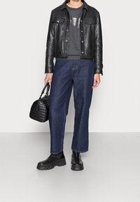 Chaqueta de cuero negra sobre un sudadera gris con un gráfico, combinada con unos vaqueros anchos y botas negras Chunky. El accesorio es un pequeño bolso negro.