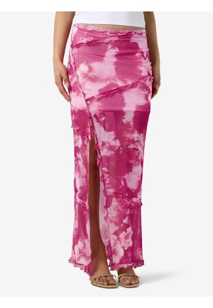 Vrouw draagt een high waist maxi rok in roze en wit tie-dye, met een voorsplit en ruches, gecombineerd met beige sandalen.