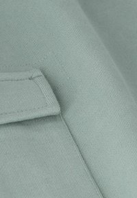 Tissu en coton bleu clair présentant une texture lisse, avec un détail de poche cousue et des coutures horizontales, offrant une surface douce et uniforme.