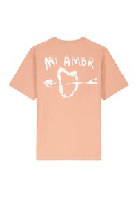 T-shirt en coton de couleur pêche avec des manches courtes. Présente un texte graphique blanc "Mi Amor" et un cœur avec une flèche dans le dos.
