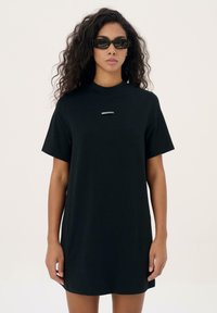 Zwarte katoenen t-shirtjurk met korte mouwen, ronde halslijn en geborduurd logo in het wit in het midden. Zachte textuur, casual pasvorm.