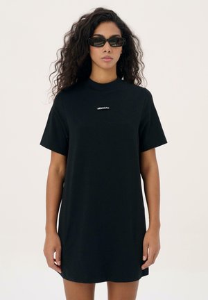 Zwarte katoenen t-shirtjurk met korte mouwen, ronde halslijn en geborduurd logo in het wit in het midden. Zachte textuur, casual pasvorm.