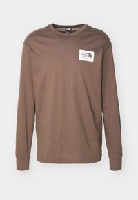 Braunes, langärmliges T-Shirt aus Baumwolle. Hat einen Rundhalsausschnitt und ein weißes Logopatch auf der linken Brust. Weicher Stoff, lässige Passform.