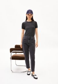 Black short-sleeve t-shirt, gray high-waisted jeans, black and white shoes, and a navy baseball cap with a logo, next to a brown chair.