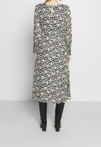 Vestido midi floral con mangas largas, fondo negro, flores en tonos crema y azul, detalle de abertura en la espalda, combinado con botas negras hasta la rodilla.