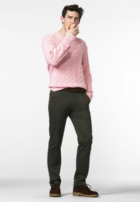 Pull en tricot rose, pantalon vert foncé, chaussures en daim marron. Modèle tenant une pomme, se tenant devant un fond clair.