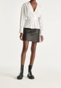 Vit blus med en omslagdesign och långa ärmar, kombinerad med en svart läderminikjol med två framfickor. Svarta ankle boots fulländar outfiten.