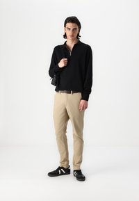 Crna dug sleeves polo majica s zatvaračem, bež chinos hlače, crne tenisice s bijelim detaljima i mala crna torbica preko ramena.