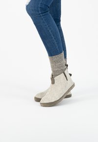 Lichtgrijze vilten enkellaarzen met bruine leren accenten, zachte textuur bovenwerk, platte zool en elastische zijtrim. Gecoördineerd met ribbelige grijze sokken.