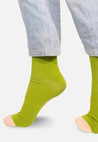 Zielona skarpetka do kostki z jasnoróżowym palcem. Wykonana z gładkiego, elastycznego materiału. Nosi się ją z jasnoniebieskimi skróconymi dżinsami.