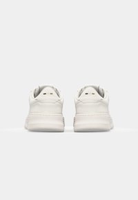 White sneakers with a smooth leather upper, rounded toe, padded collar, and a textured rubber sole. Minimalist design, subtle branding details.