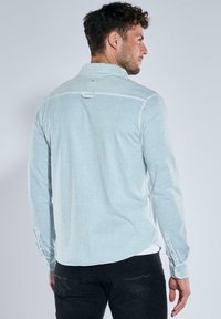 Light blue long-sleeve shirt with a button-down collar, featuring a back yoke and a subtle texture. Styled with dark gray pants.