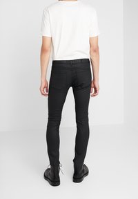 Jean ajustados negros con bolsillos traseros, una textura suave y un diseño ajustado, combinados con una camiseta blanca lisa y botas negras.