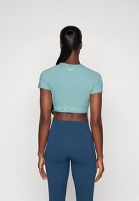 Camiseta de manga corta Nike Pro en teal claro, con material transpirable, un diseño cropped y el logo reflectante "NIKE PRO" en la parte posterior.