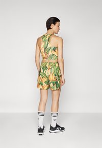 Floral-patterned activewear set featuring a cropped top and shorts in yellow and green hues. Black sneakers and white striped socks included.