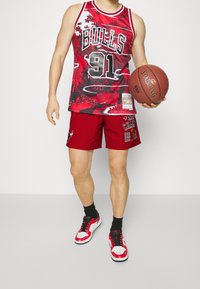 Röd baskettröja med svarta och vita detaljer, med texten "BULLS" och "91". Matcher med röda shorts och svarta sneakers.