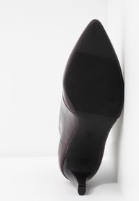 Chaussure à talon haut en cuir bordeaux avec un bout pointu et une semelle en caoutchouc noire texturée. Marquée « 37 » sur la semelle.