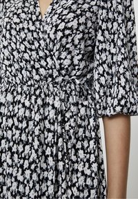 Robe portefeuille florale noir et blanc avec un tissu plissé, des manches courtes bouffantes, une taille à nouer et un décolleté en V profond.
