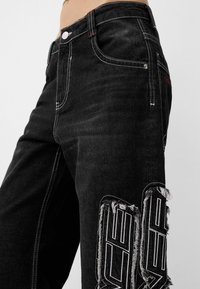 Musta farkut, joissa on kontrastivalkoinen tikkaus. Ominaisuuksina repaleiset yksityiskohdat ja rohkeat graafiset aksentit alavarpaan kohdalla. Klassinen viiden taskun muotoilu.