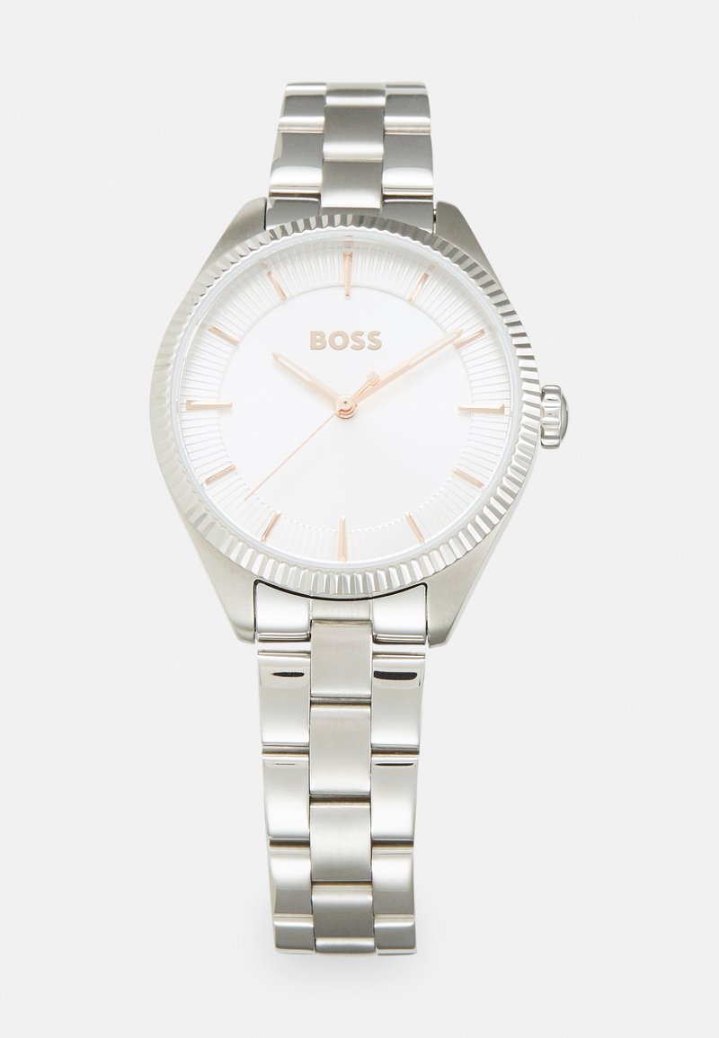 Sølvklokke med en teksturert hvit skive og rose gull detaljer. Har en armbånd av rustfritt stål og en ribbet bezel.