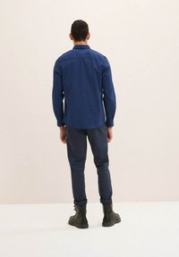 Camicia a manica lunga a quadri blu, abbinata a pantaloni blu navy e stivali neri stringati. Presenta un colletto classico e polsini con bottoni.