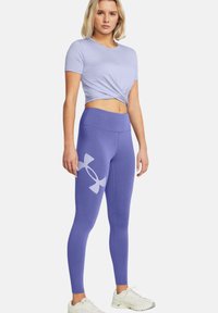 Top corto de manga corta lila anudado en la cintura, combinado con leggings morados de cintura alta y ajustados que presentan un gran logotipo blanco.