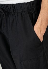 Schwarze Hose mit elastischem Bund und Kordelzug. Verfügt über Seitentaschen und ein gerades Bein-Design. Der Stoff hat eine dezente Struktur.