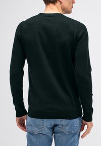Dunkelgrüner Pullover mit langen Ärmeln, gerippten Bündchen und Rundhalsausschnitt, aus einem weichen, strukturierten Stoff, kombiniert mit blauen Jeans.