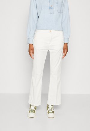 Person wearing white straight-leg pants, light blue denim shirt, and green high-top sneakers standing against a plain white background.