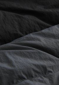 Grey textile folds, featuring a mix of dark grey and charcoal hues. The fabric has a textured, slightly wrinkled surface.