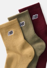 Tri par ribanastih nogavic v olivno zeleni, gorčični rumeni in burgundski barvi, z belimi izvezenimi logotipi na straneh.