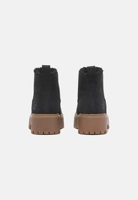 Black leather ankle boots with faux fur lining and brown ridged soles. Features a pull tab at the back and embossed logo detail.