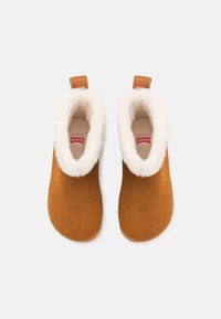 Un paio di stivali in camoscio marrone a slip-on per l'inverno, con fodera in pelliccia bianca e linguette di estrazione, mostrati dall'alto su uno sfondo bianco.