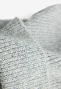Tissu tricoté gris avec une surface texturée, présentant une apparence douce et duveteuse, mettant en valeur de subtiles variations de couleur et de motif.