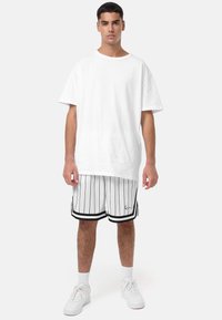 Vit bomulls-t-shirt med lös passform, tillsammans med svart-vita randiga shorts med svarta detaljer och en liten logotyp. Vita sneakers.