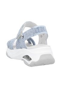 Sandales en tissu bleu clair avec un dessus texturé, une semelle intermédiaire blanche et une semelle extérieure grise. Sangles réglables pour un ajustement sûr.