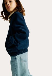 Granatowy sweatshirt z ściągaczami przy mankietach i dolnym brzegu, z teksturowanym beżowym kołnierzem, w połączeniu z jasnoniebieskimi dżinsami o wysokim stanie.