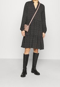 Černé květinové šaty s nabraným lemem, dlouhými rukávy a výstřihem do V. Doplněné koženými černými vysokými botami a růžovou křížovou taškou.