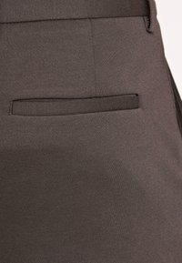 Grauer Stoff der Hose mit glatter Textur, mit einer einzelnen Paspeltasche auf der Rückseite. Einfaches und minimalistisches Design.