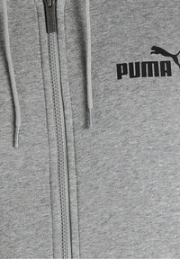 Sweat à capuche gris clair zippé avec cordons, arborant un logo PUMA noir sur la poitrine et une surface en tissu texturé. Détail de fermeture éclair argentée.