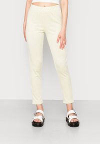 Leggings amarelos e brancos com padrão xadrez, cintura elástica, ajuste slim e textura suave, combinados com sandálias brancas chunky.